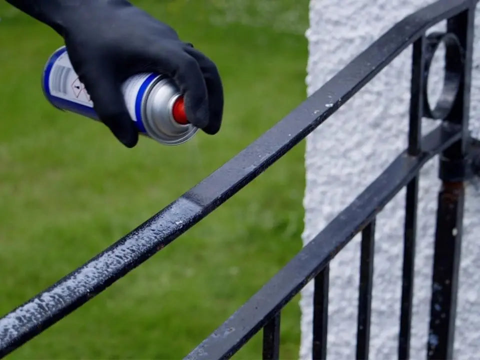 Hand wearing a black glove applying a white substance to a metal railing.